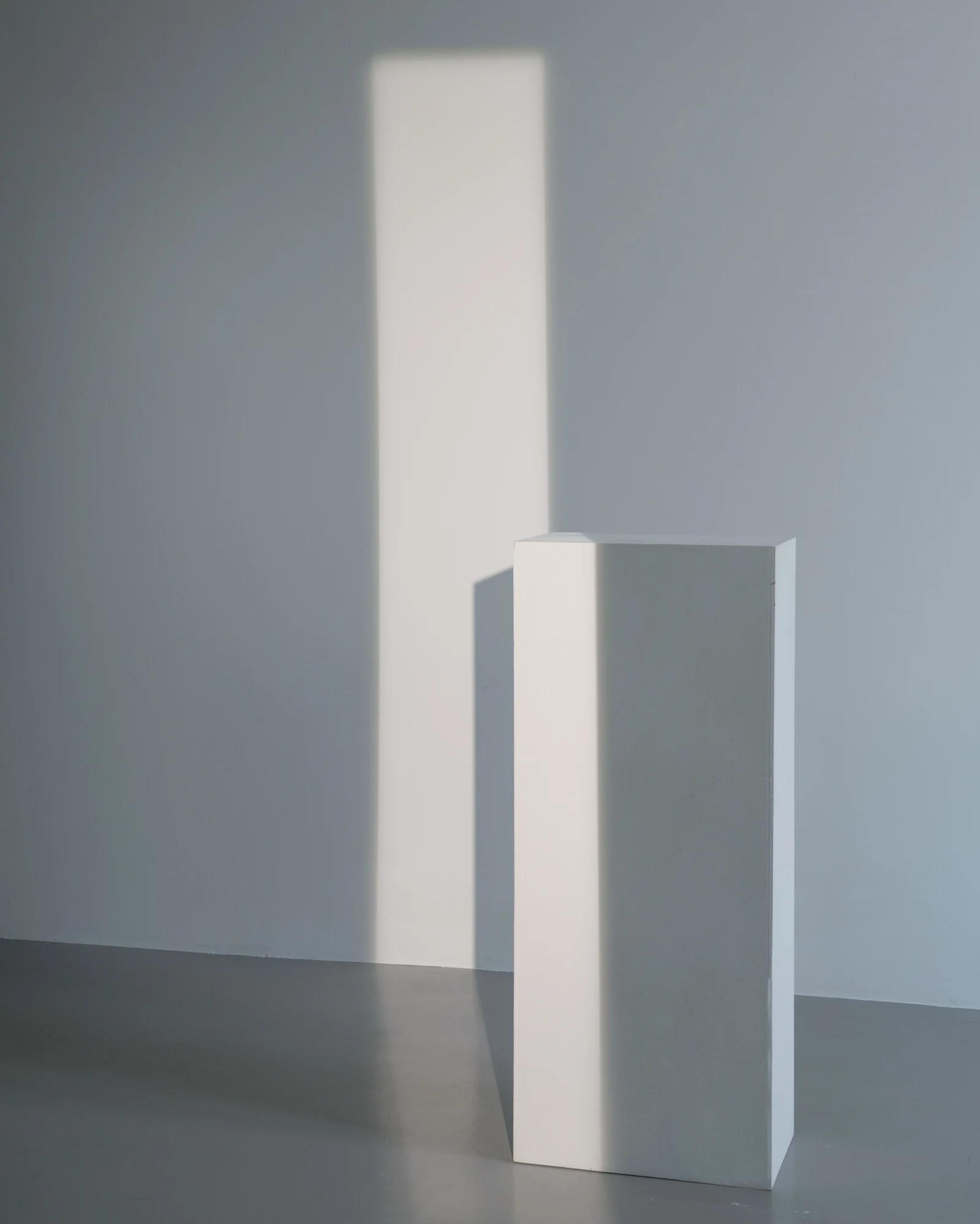 Colonne isolée dans une pièce blanche baignée de lumière.