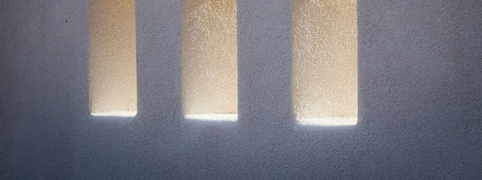 Trois ouvertures rectangulaires dans un mur de béton éclairé par le soleil.